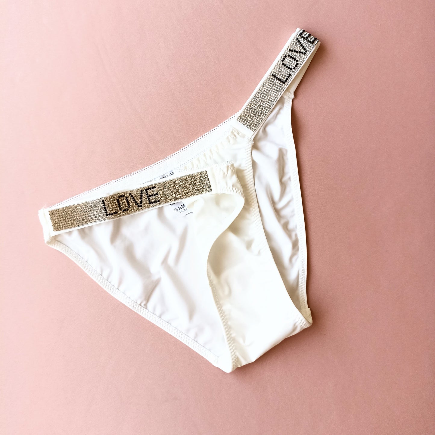 Lygios kelnaitės stringai su blizgiais šoneliais "LOVE", pieno balta, kūno (L-XL)