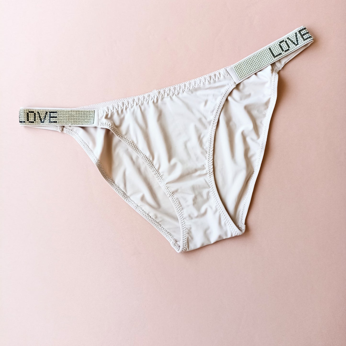 Lygios kelnaitės stringai su blizgiais šoneliais "LOVE", pieno balta, kūno (L-XL)